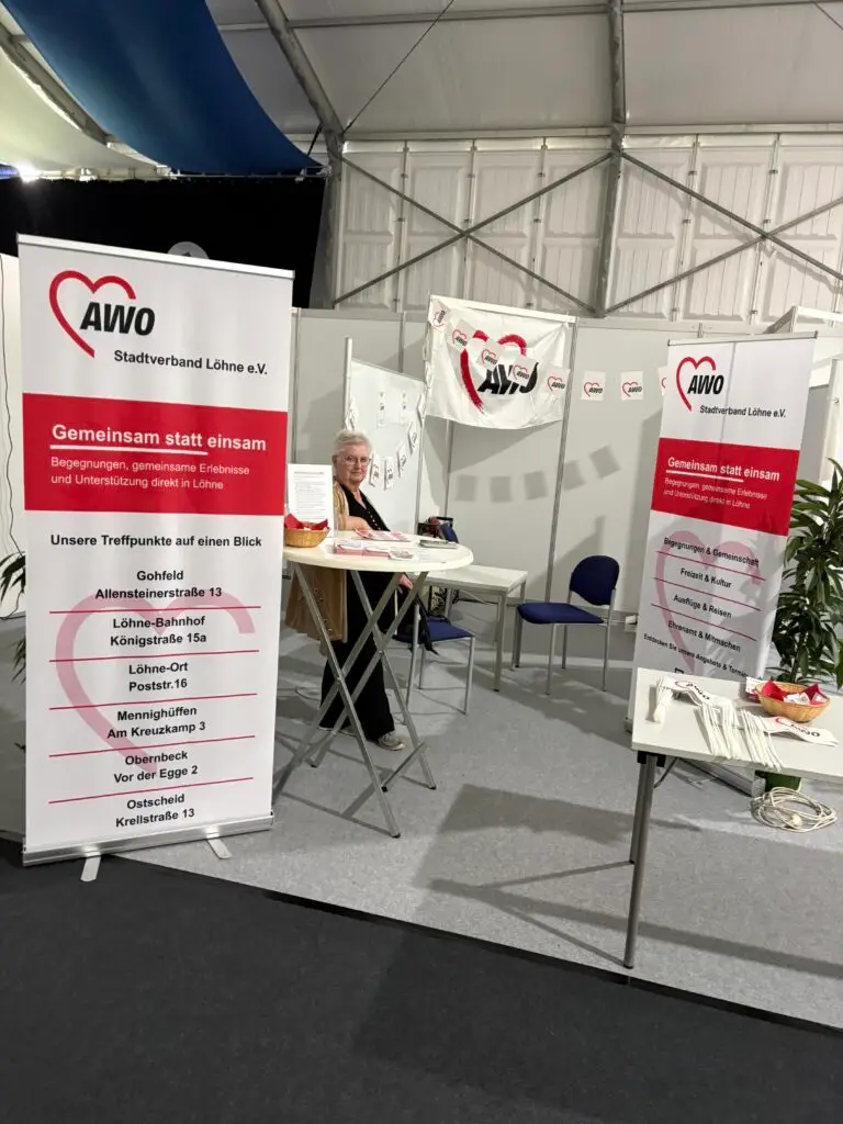 Eine Frau am Stehtisch des AWO-Informationsstands mit Flyern, AWO-Fahne und Roll-ups auf der Gewerbeschau 2026.