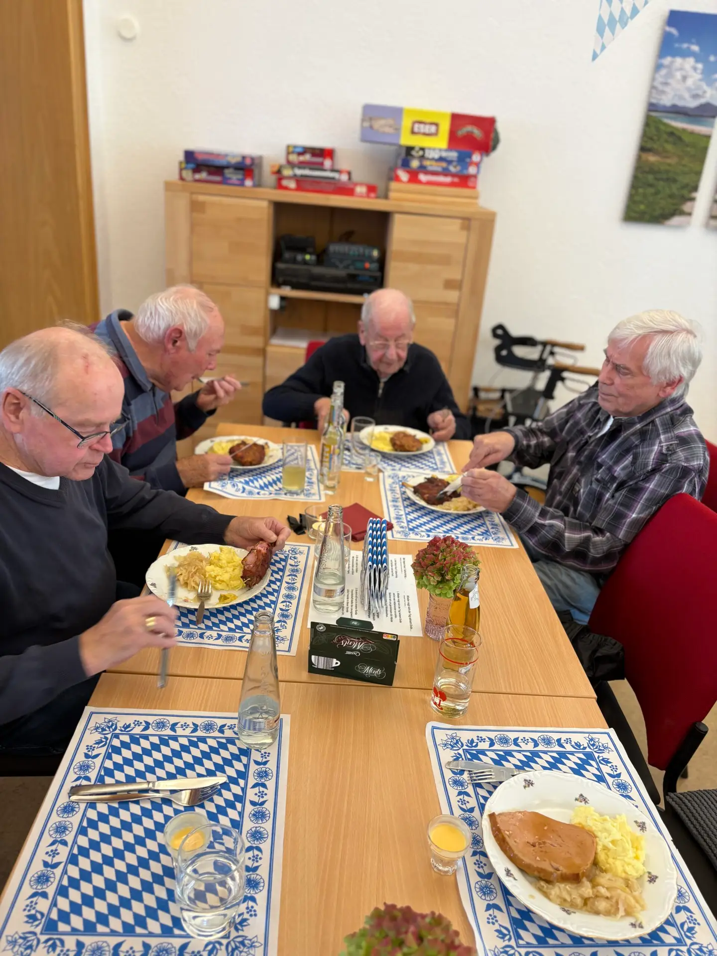 Ältere Männer essen gemeinsam an einem blau-weiß gedeckten Tisch