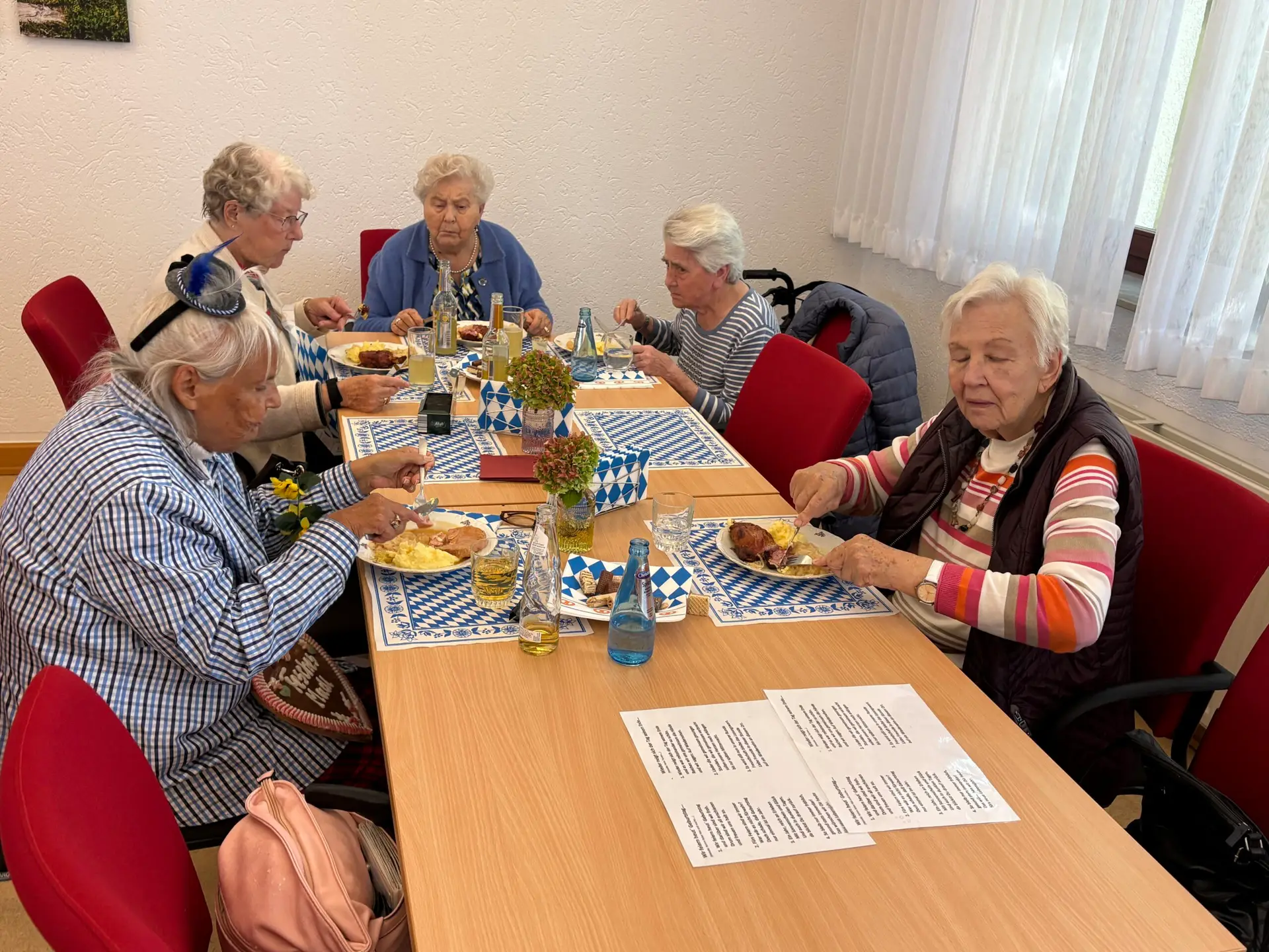 Seniorinnen essen an einem Tisch mit blau-weißen Platzsets und Liedzetteln
