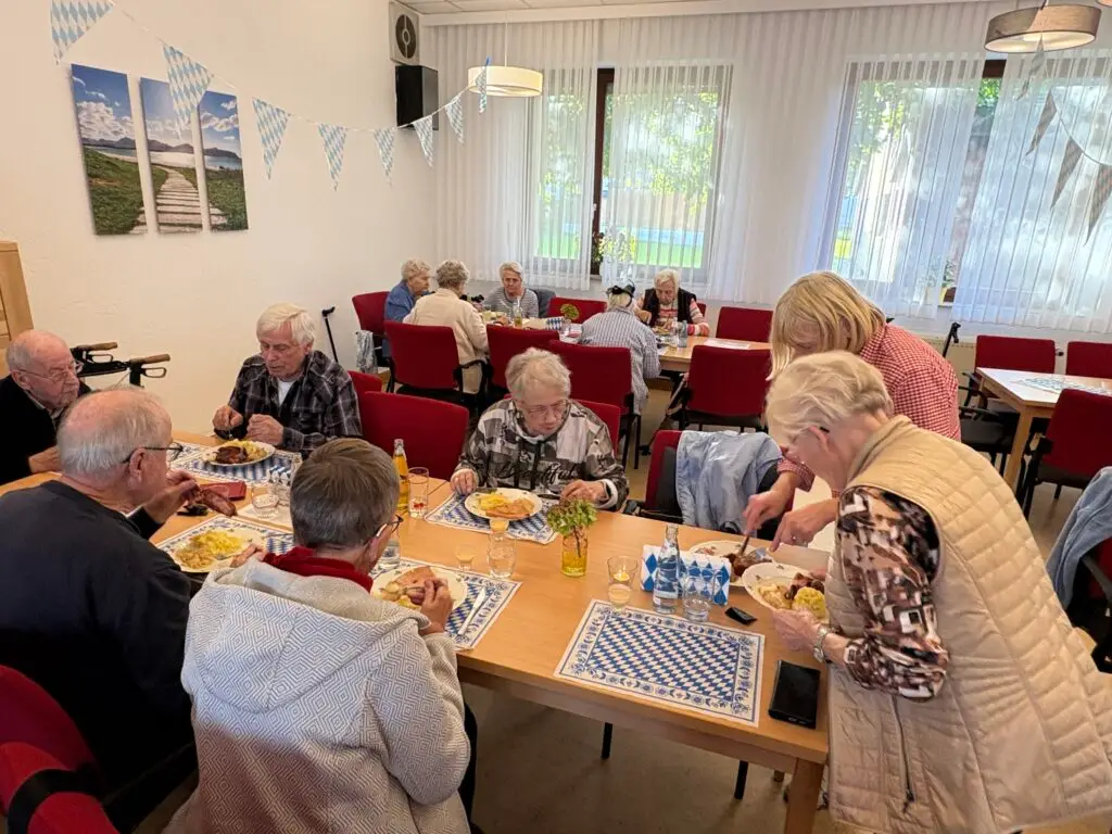 Geschmückter Raum mit blau-weißen Wimpeln, Gäste essen an mehreren Tischen