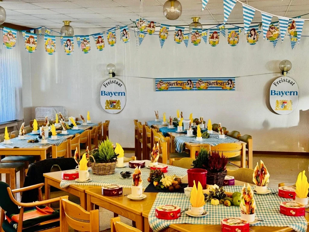 Festlich gedeckte Tische mit blau-weiß karierten Tischläufern und gelben Servietten, darüber Wimpelketten, an der Wand Schilder „Freistaat Bayern“