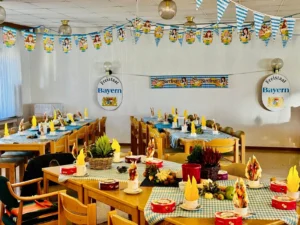 Festlich gedeckte Tische mit blau-weiß karierten Tischläufern und gelben Servietten, darüber Wimpelketten, an der Wand Schilder „Freistaat Bayern“