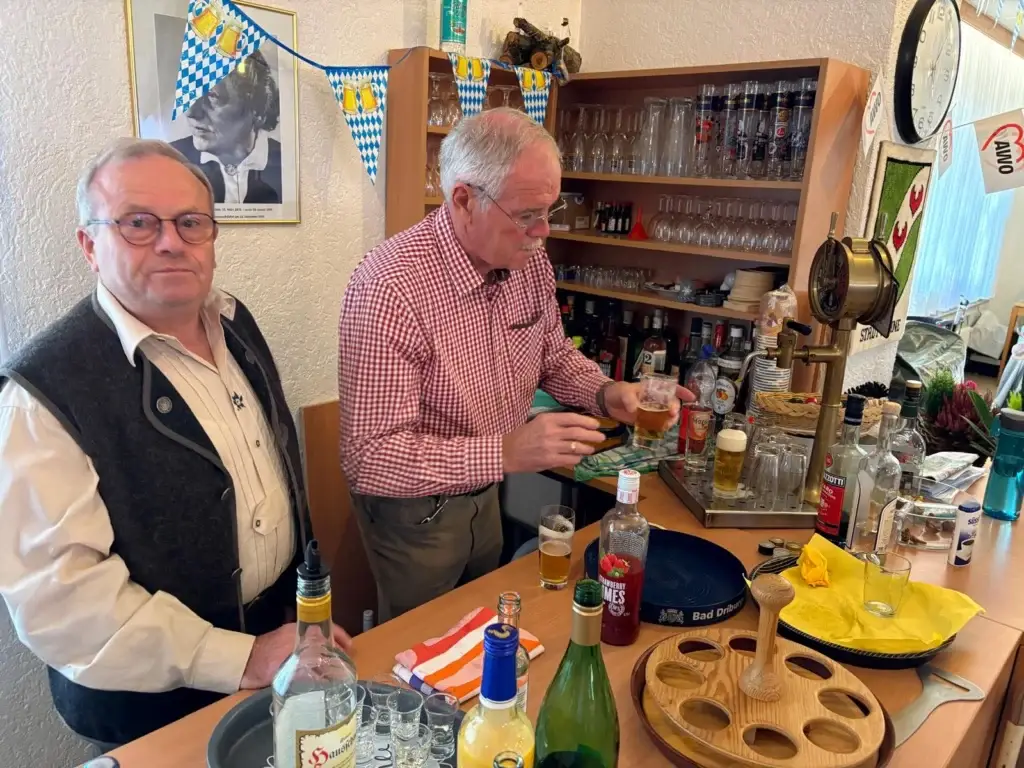 Zwei Männer in Trachtenweste und kariertem Hemd an der Theke, einer hält ein frisch gezapftes Bier