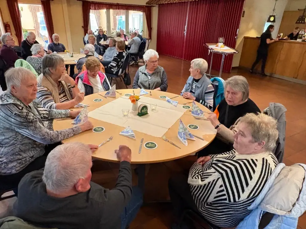 Gäste sitzen an runden, gedeckten Tischen in einem Gastraum mit roten Vorhängen