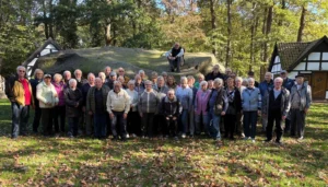 Große Gruppe von Seniorinnen und Senioren auf einer Wiese mit Herbstlaub vor dem Großen Stein von Tonnenheide, ein Mann sitzt oben auf dem Findling