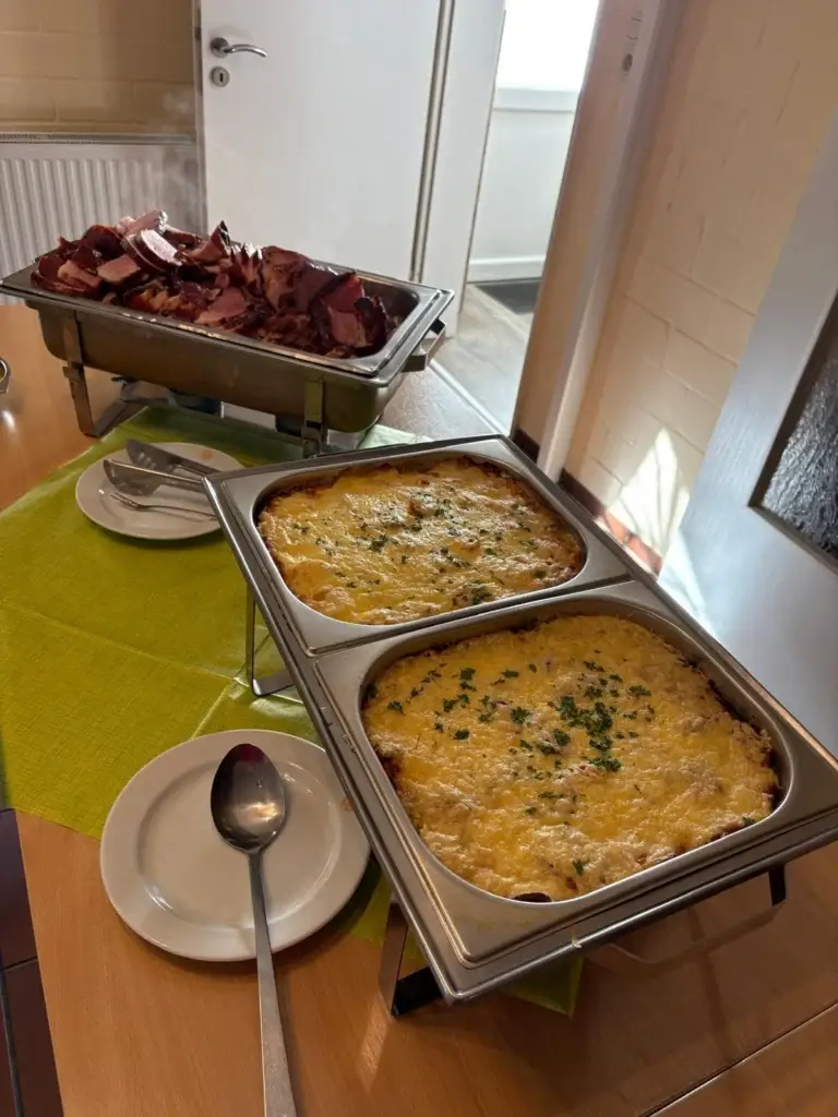 Buffet mit Spießbraten und zwei Formen mit überbackenem Auflauf in Warmhaltebehältern