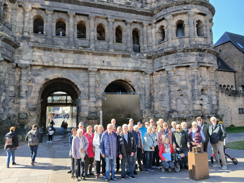 Die Reisegruppe des AWO Stadtverbands Löhne steht vor der Porta Nigra in Trier, einem großen römischen Stadttor aus dunklem Sandstein
